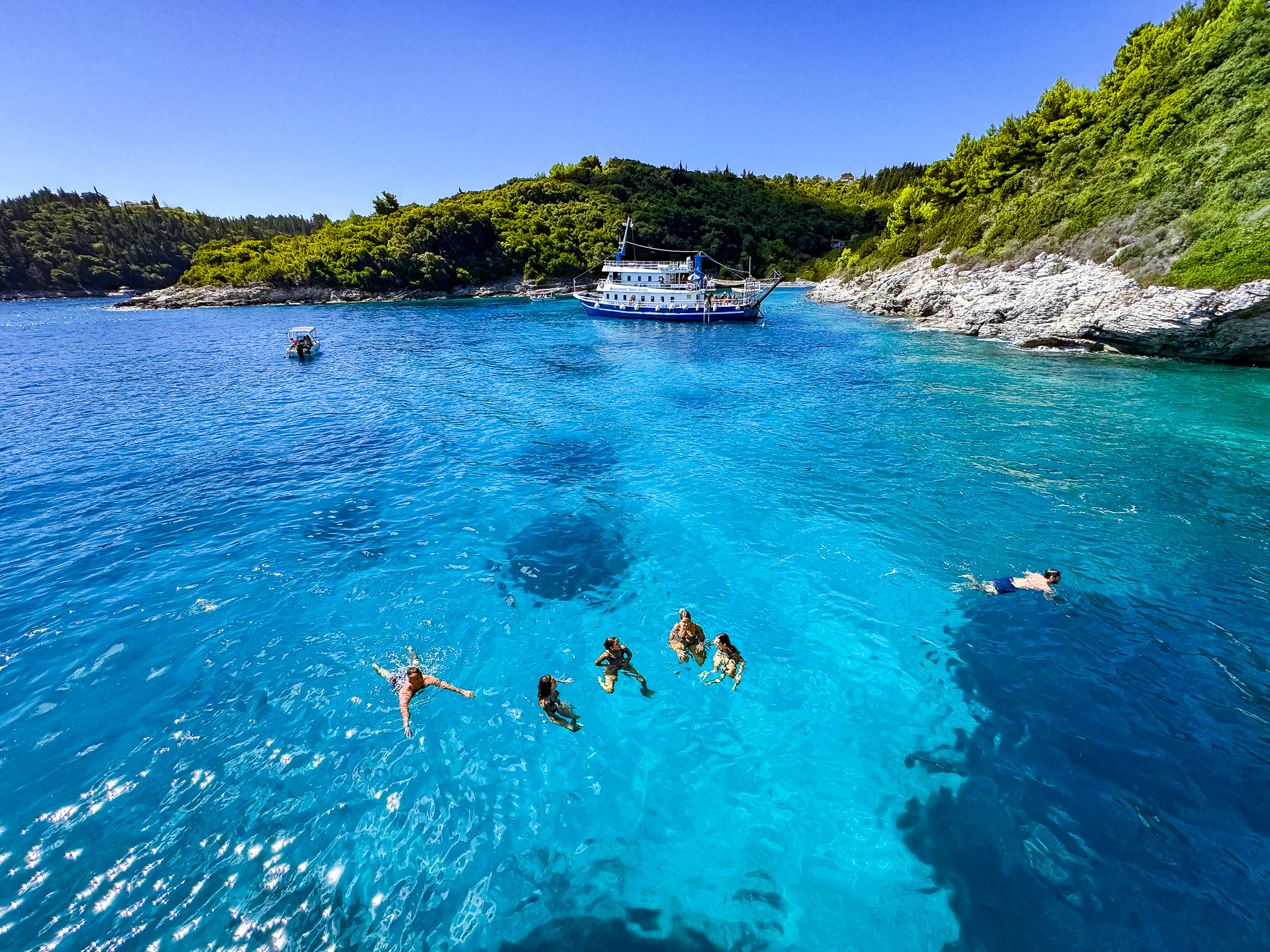Turyści pływający w turkusowym morzu przy wyspie Antipaxos w Grecji